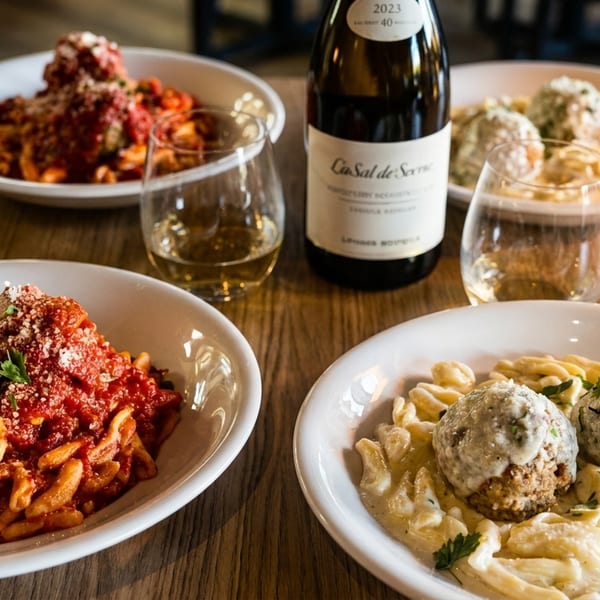 Two pasta dishes with meatballs, one with red sauce and one with cream sauce, alongside white wine.