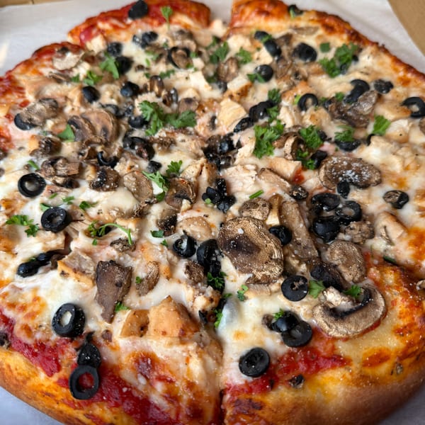 Cheesy pizza topped with mushrooms, black olives, chicken, and fresh parsley in a cardboard box.