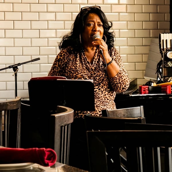 A woman in a leopard print top sings into a microphone on a stage with an accordion.