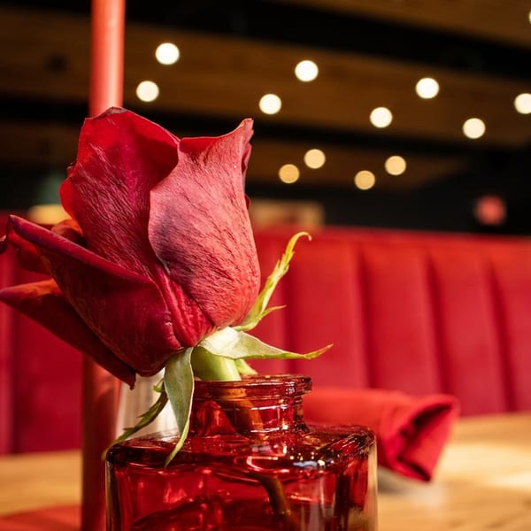A single red rose in a red vase on a table with red booth seating in the background.