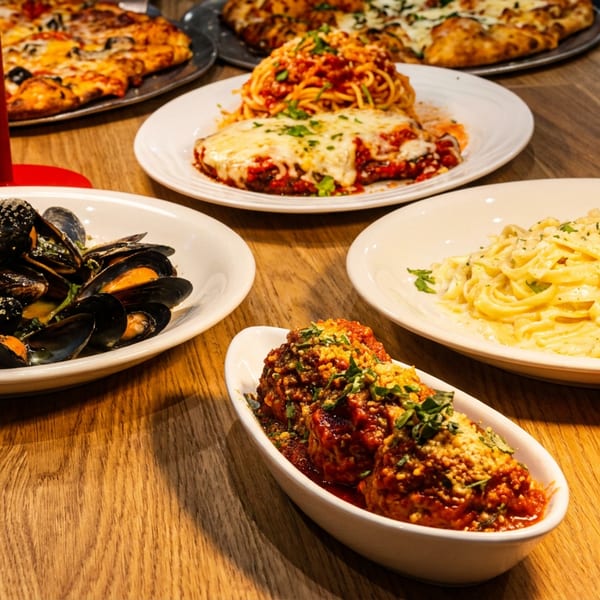 A wooden table laden with various Italian dishes, including pizza, pasta, mussels, and meatballs.