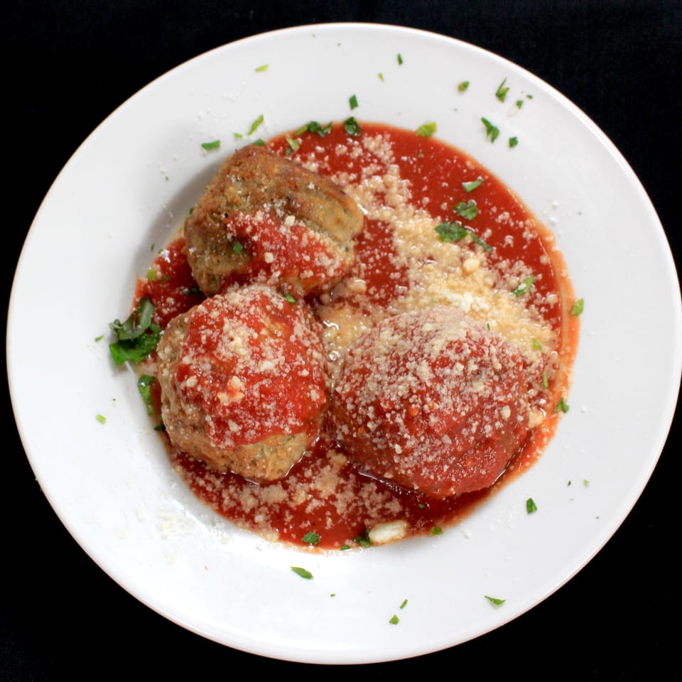 Breaded eggplant slices layered with tomato sauce, grated cheese, and parsley on a white plate.