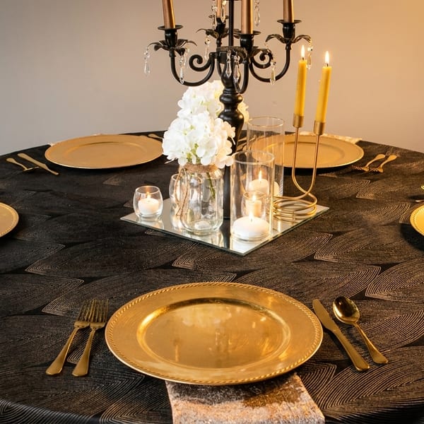 Elegant round dining table set with gold plates, cutlery, and a candelabra centerpiece.