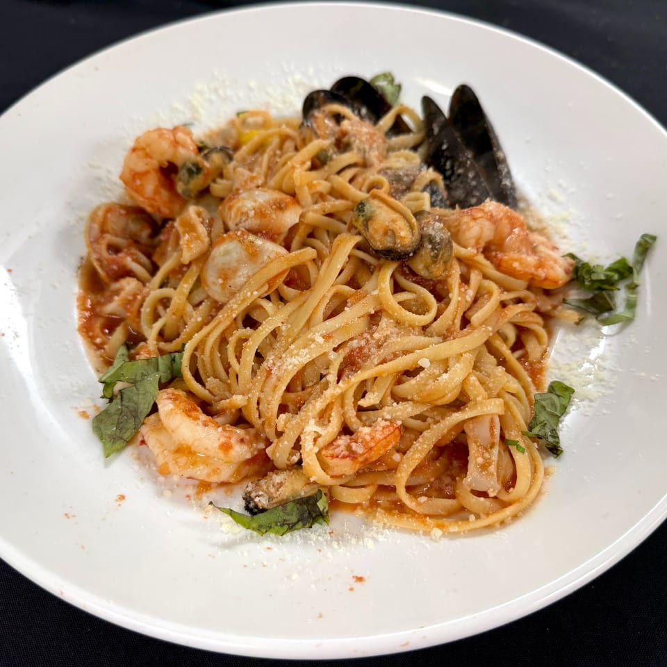 Seafood linguine with shrimp, mussels, tomato sauce, herbs, and grated cheese served on a white plate.