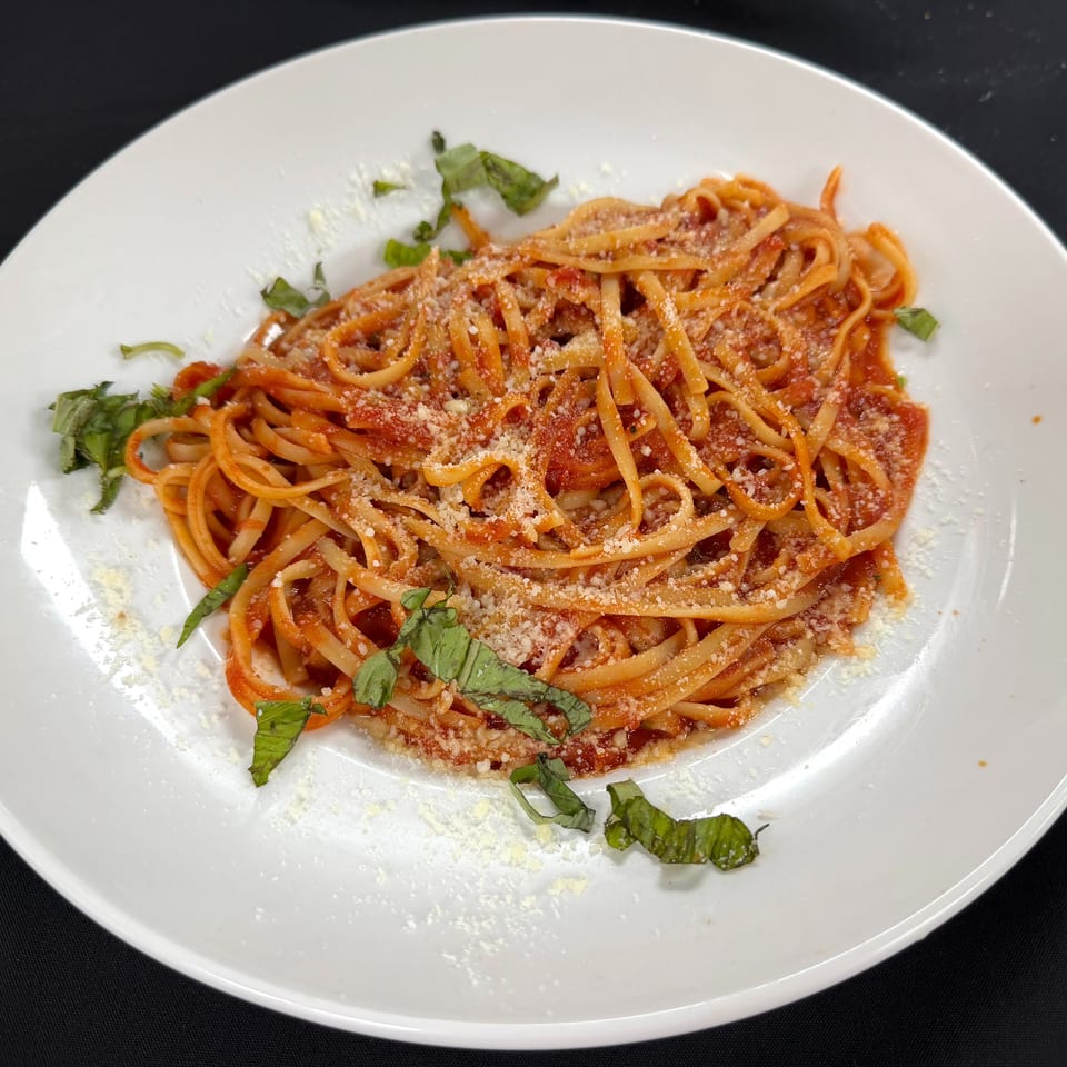 Linguine coated in tomato sauce, topped with grated Parmesan and fresh basil on a white plate.