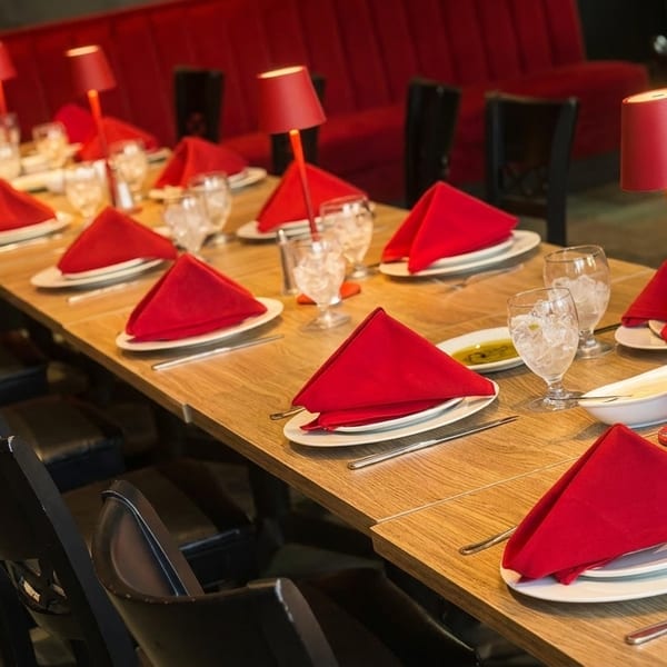 Long dining table set with red napkins, white plates, and red table lamps in a restaurant.