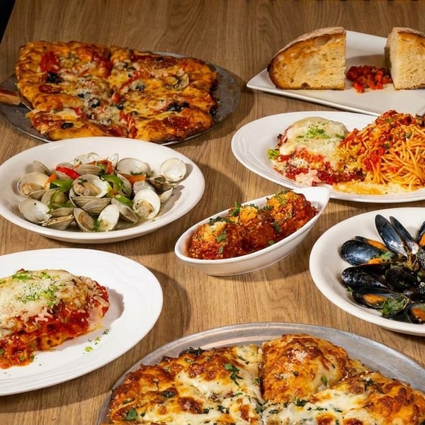 A wooden table laden with various Italian dishes, including pizzas, pasta, meatballs, clams, and mussels.